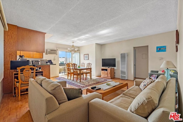 living room with a wall mounted AC, a chandelier, light hardwood / wood-style flooring, and a textured ceiling