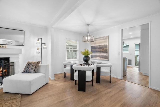 dining space with ornamental molding, plenty of natural light, a fireplace, and light hardwood / wood-style flooring