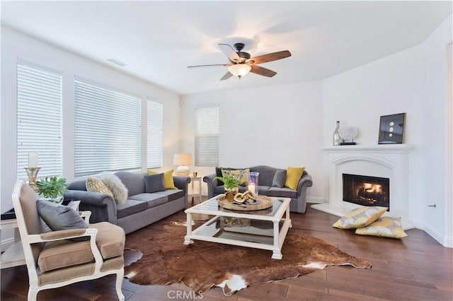 living room featuring baseboards, visible vents, a glass covered fireplace, ceiling fan, and wood finished floors