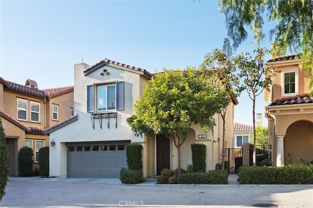 mediterranean / spanish-style home featuring driveway, an attached garage, a tile roof, and stucco siding