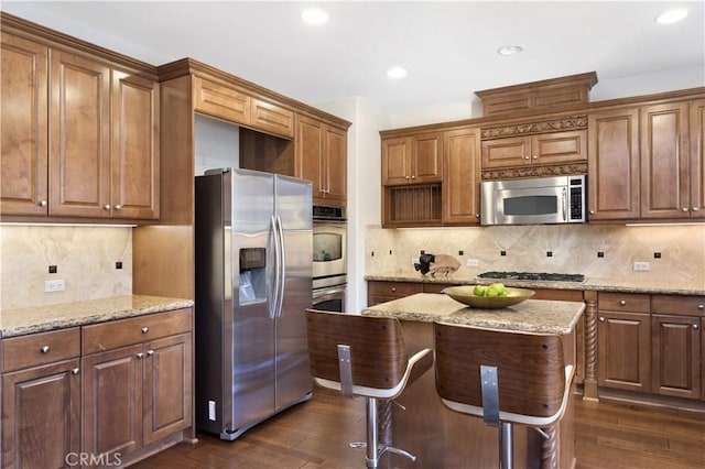 kitchen with a kitchen island, appliances with stainless steel finishes, backsplash, dark hardwood / wood-style flooring, and light stone countertops