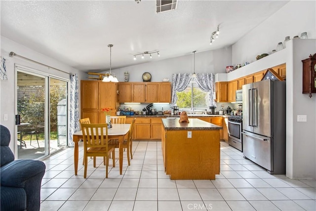 kitchen featuring hanging light fixtures, a kitchen island, stainless steel appliances, light tile patterned flooring, and vaulted ceiling