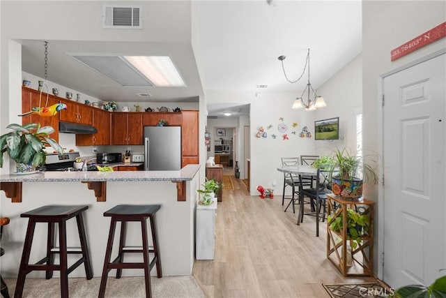 kitchen featuring decorative light fixtures, a kitchen breakfast bar, light hardwood / wood-style floors, kitchen peninsula, and stainless steel appliances