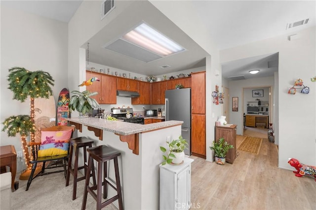 kitchen with appliances with stainless steel finishes, a kitchen breakfast bar, kitchen peninsula, and light hardwood / wood-style floors