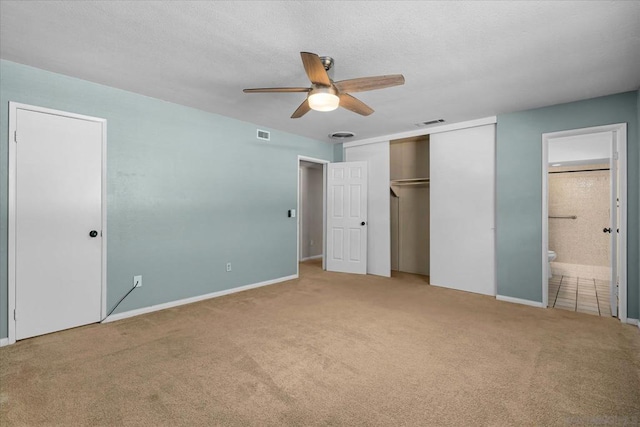 unfurnished bedroom featuring ceiling fan, light colored carpet, a textured ceiling, and ensuite bath