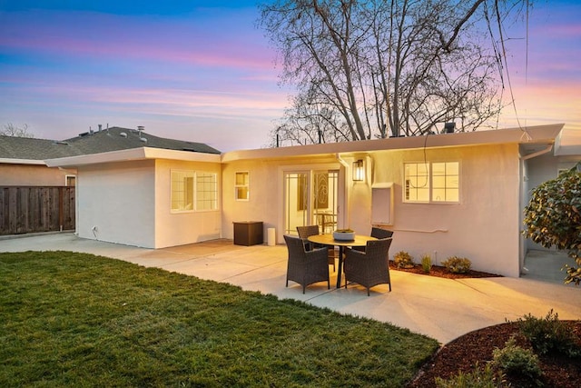 back house at dusk featuring a lawn and a patio