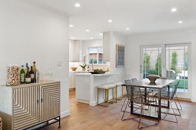 dining space featuring indoor bar, ornamental molding, and light wood-type flooring