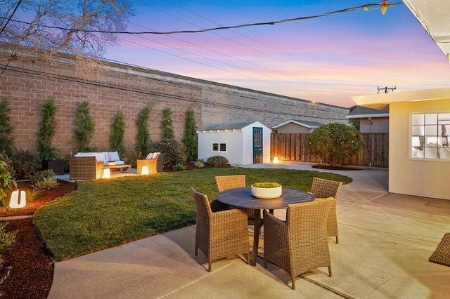 patio terrace at dusk with a shed, an outdoor living space, and a yard