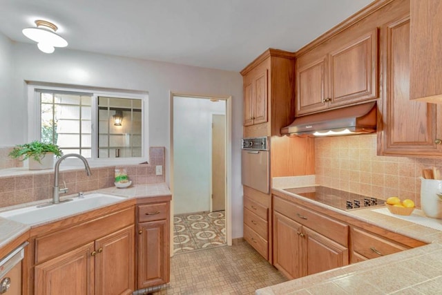 kitchen featuring tile countertops, sink, backsplash, black electric stovetop, and wall oven