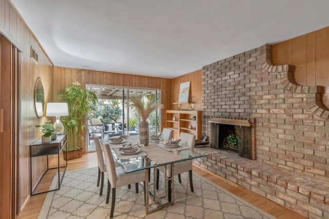 dining area with a fireplace, wooden walls, and light hardwood / wood-style floors