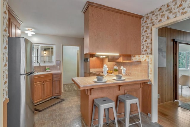 kitchen featuring a breakfast bar, stainless steel refrigerator, sink, backsplash, and kitchen peninsula