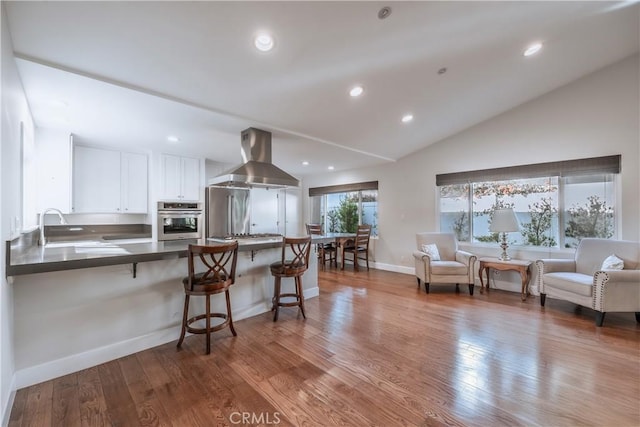 kitchen with sink, white cabinetry, island range hood, appliances with stainless steel finishes, and kitchen peninsula