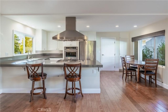 kitchen with island range hood, stainless steel appliances, a kitchen bar, and white cabinets