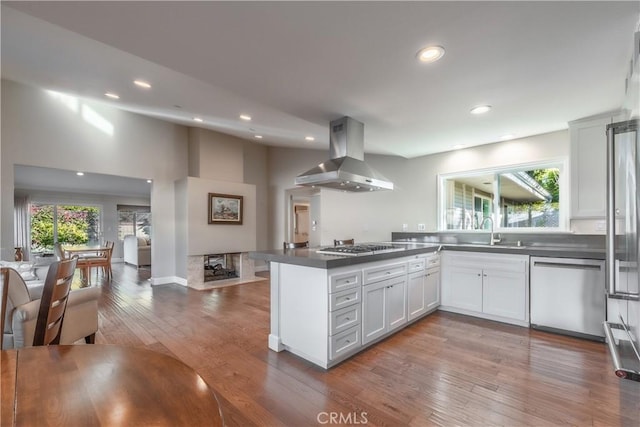 kitchen featuring sink, stainless steel appliances, island range hood, white cabinets, and kitchen peninsula