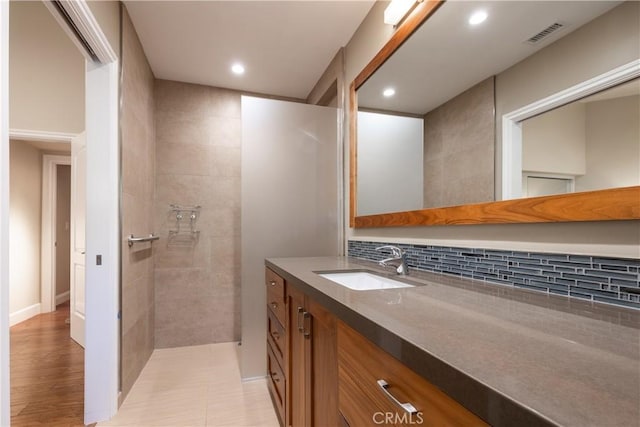 bathroom featuring vanity, a tile shower, and backsplash