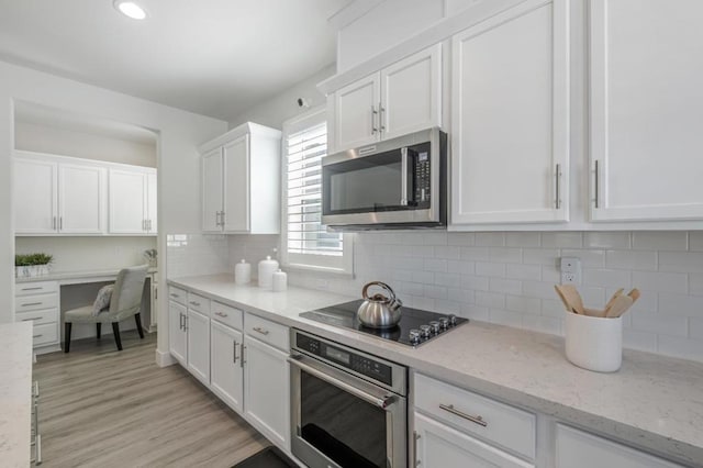 kitchen featuring built in desk, tasteful backsplash, white cabinetry, light stone counters, and stainless steel appliances