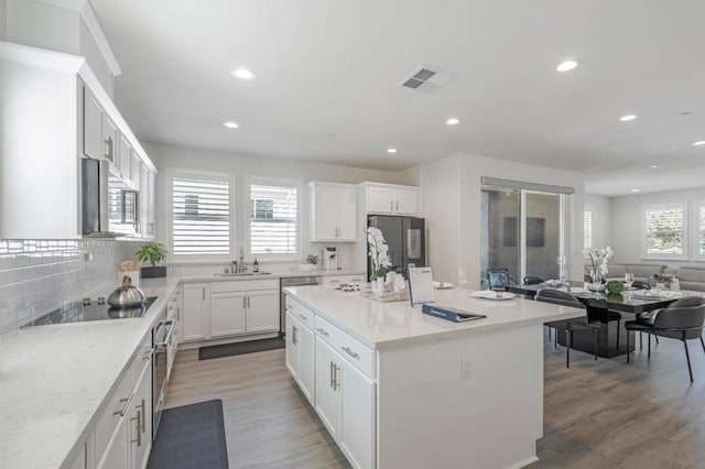 kitchen featuring sink, appliances with stainless steel finishes, a center island, light stone counters, and white cabinets