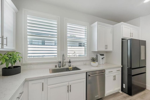 kitchen featuring sink, black refrigerator, dishwasher, light stone countertops, and white cabinets