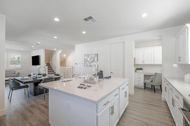 kitchen with light hardwood / wood-style flooring, light stone countertops, a kitchen island, and white cabinets