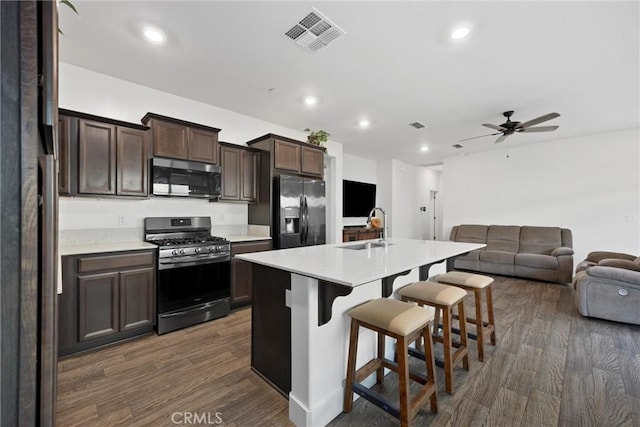 kitchen with appliances with stainless steel finishes, dark hardwood / wood-style floors, an island with sink, sink, and a kitchen bar