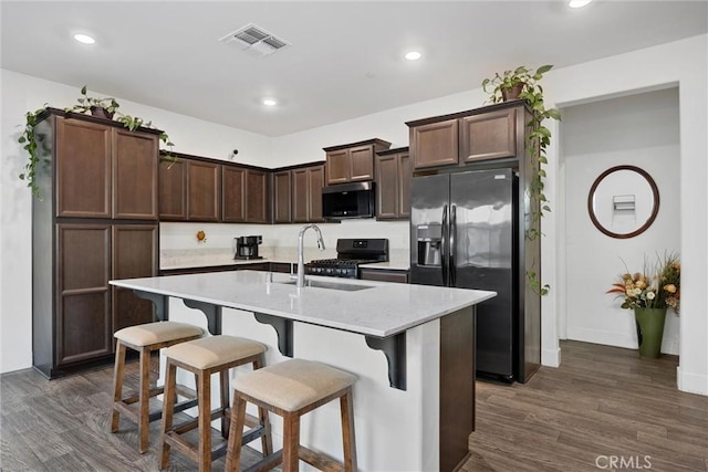 kitchen with sink, stove, light stone counters, stainless steel refrigerator with ice dispenser, and a center island with sink