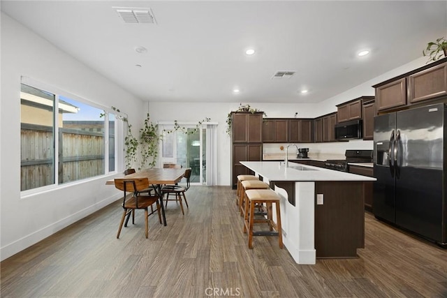 kitchen with dark hardwood / wood-style flooring, sink, a center island with sink, and black appliances