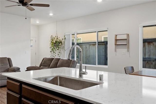 kitchen with light stone counters, ceiling fan, sink, and hardwood / wood-style floors