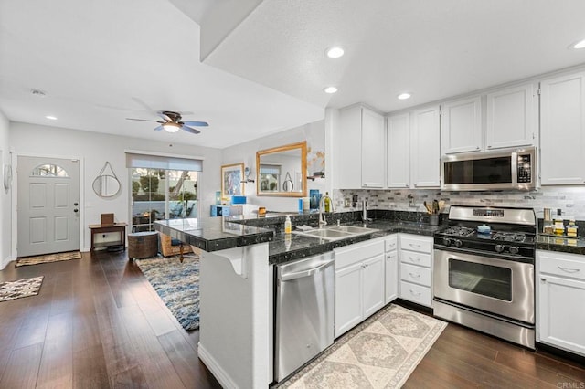 kitchen featuring sink, appliances with stainless steel finishes, white cabinetry, dark hardwood / wood-style floors, and kitchen peninsula