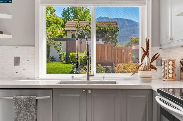 kitchen featuring gray cabinetry, sink, backsplash, and stainless steel dishwasher