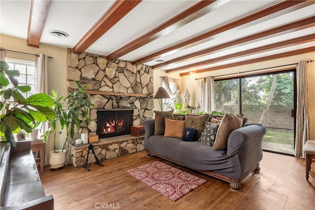 living room with beamed ceiling, a stone fireplace, and light hardwood / wood-style floors