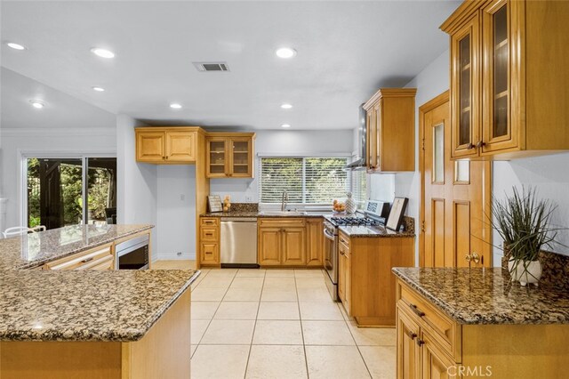 kitchen with sink, light tile patterned floors, appliances with stainless steel finishes, ornamental molding, and stone countertops