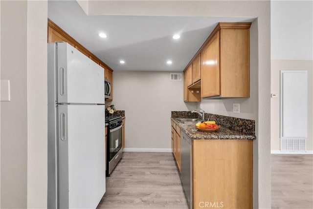 kitchen featuring dark stone countertops, sink, light hardwood / wood-style floors, and appliances with stainless steel finishes