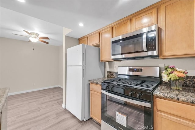 kitchen with light brown cabinetry, light wood-type flooring, appliances with stainless steel finishes, ceiling fan, and dark stone counters