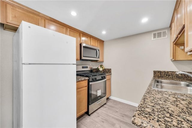 kitchen featuring appliances with stainless steel finishes, sink, light wood-type flooring, and dark stone counters