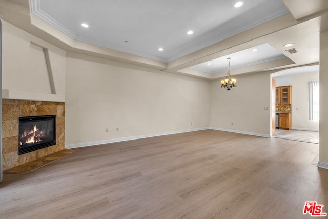 unfurnished living room with crown molding, a chandelier, a tray ceiling, a premium fireplace, and light wood-type flooring