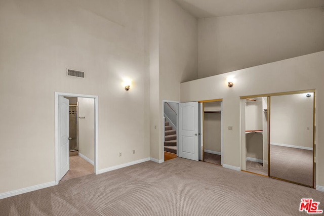 unfurnished bedroom with a high ceiling, ensuite bathroom, two closets, and light colored carpet