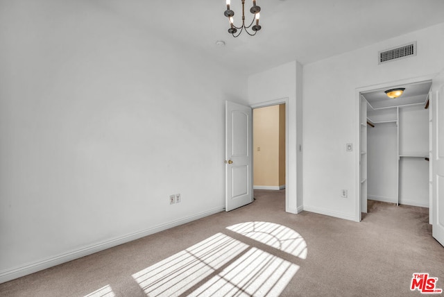 unfurnished bedroom featuring a walk in closet, light colored carpet, an inviting chandelier, and a closet