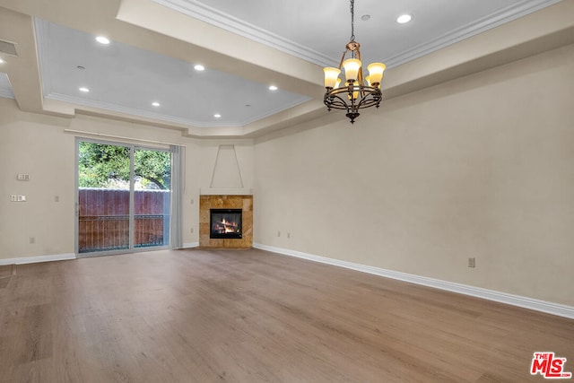 unfurnished living room with a raised ceiling, a tiled fireplace, ornamental molding, and light wood-type flooring