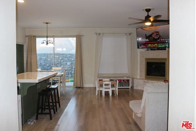 dining area featuring dark hardwood / wood-style floors, a premium fireplace, and ceiling fan with notable chandelier