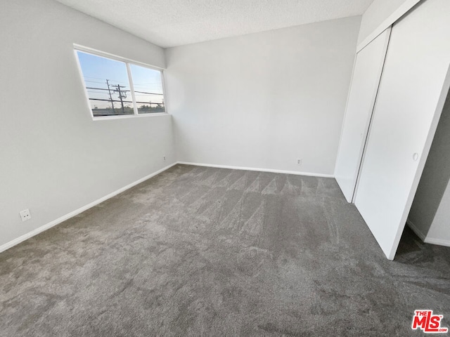 unfurnished bedroom featuring a textured ceiling, dark carpet, and a closet