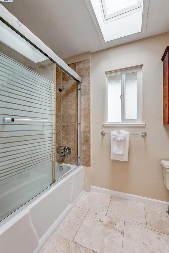 bathroom featuring toilet, a skylight, and combined bath / shower with glass door