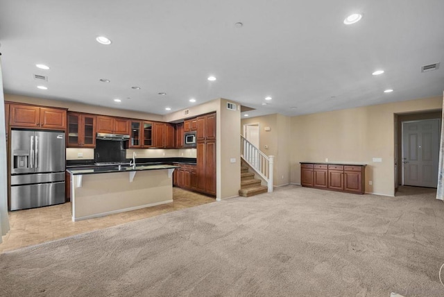 kitchen featuring sink, appliances with stainless steel finishes, a kitchen breakfast bar, a center island with sink, and light carpet