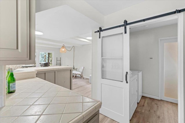 interior space featuring washing machine and clothes dryer, a barn door, tile countertops, and light wood-type flooring