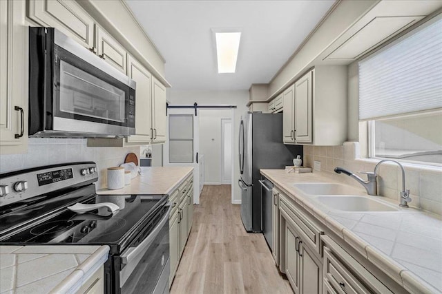 kitchen featuring appliances with stainless steel finishes, sink, backsplash, a barn door, and light hardwood / wood-style flooring