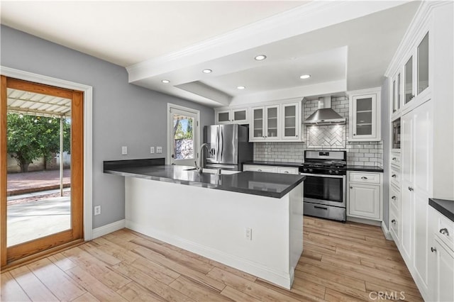 kitchen with wall chimney range hood, stainless steel appliances, light hardwood / wood-style floors, white cabinets, and kitchen peninsula