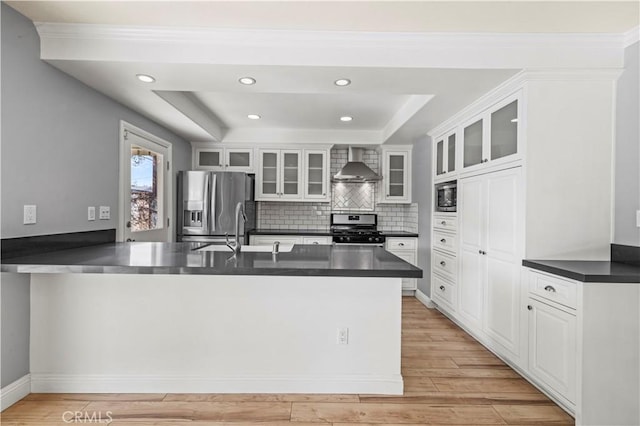 kitchen with wall chimney exhaust hood, stainless steel appliances, kitchen peninsula, and white cabinets