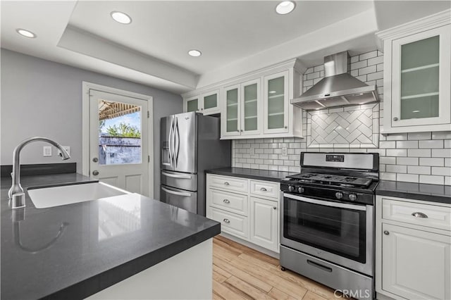 kitchen featuring sink, white cabinetry, appliances with stainless steel finishes, decorative backsplash, and wall chimney range hood