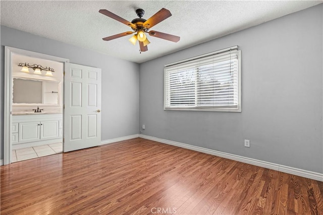 unfurnished bedroom with ensuite bathroom, sink, a textured ceiling, and light hardwood / wood-style floors