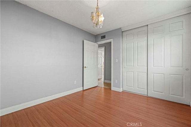 unfurnished bedroom with hardwood / wood-style flooring, a chandelier, and a closet