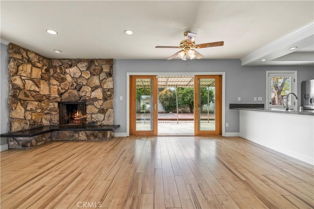 unfurnished living room featuring a stone fireplace, sink, ceiling fan, and light hardwood / wood-style flooring